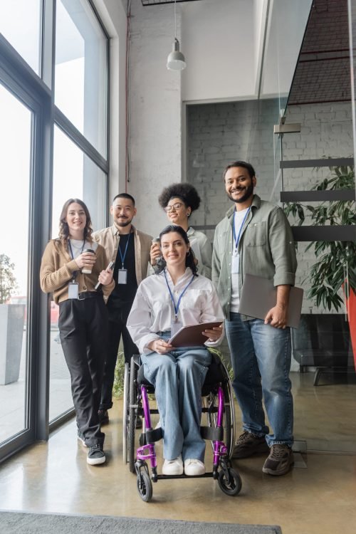 group shot of diverse startup team looking at camera in office, wheelchair user, inclusion concept